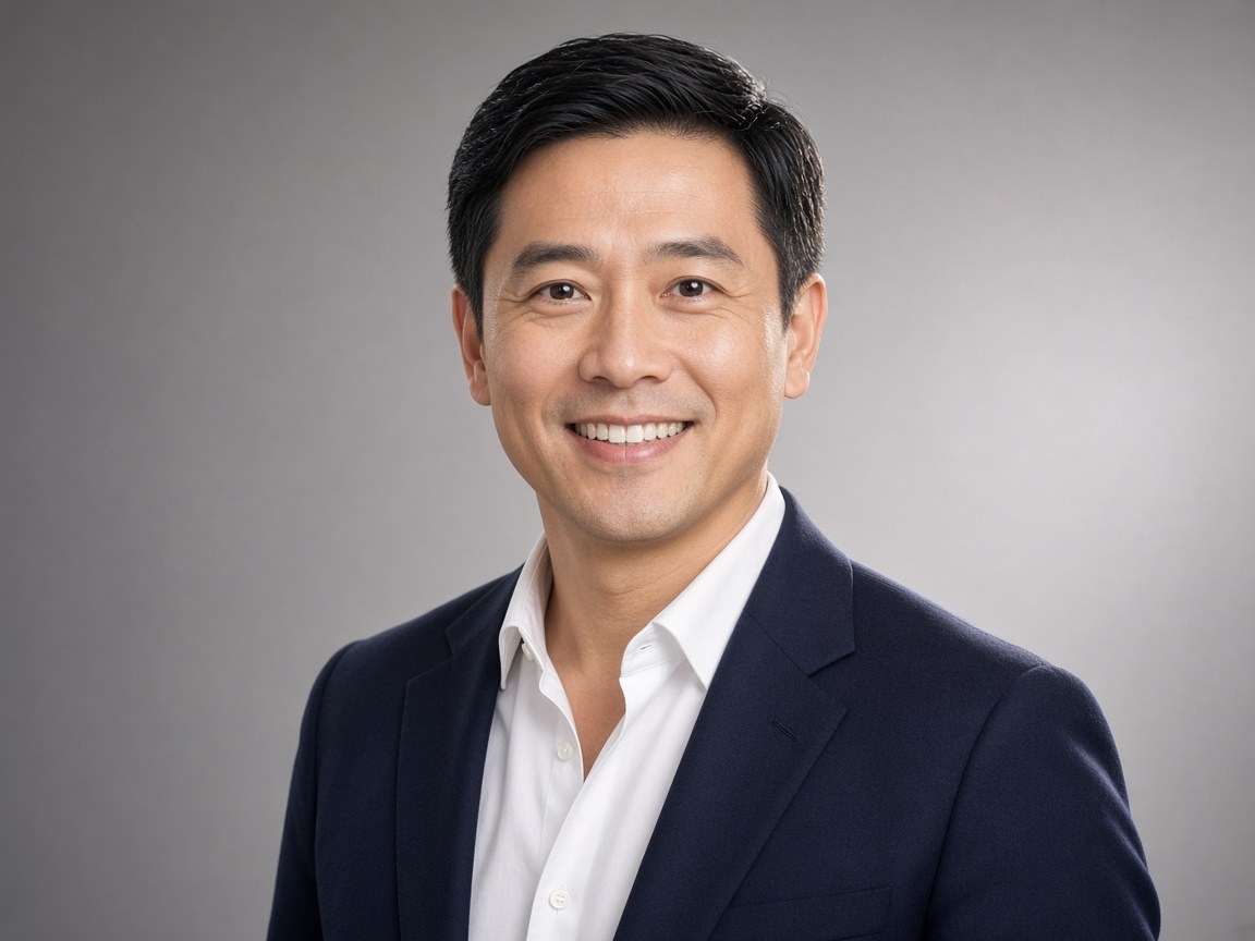 A professional headshot of a man in a navy blazer on a gray studio background