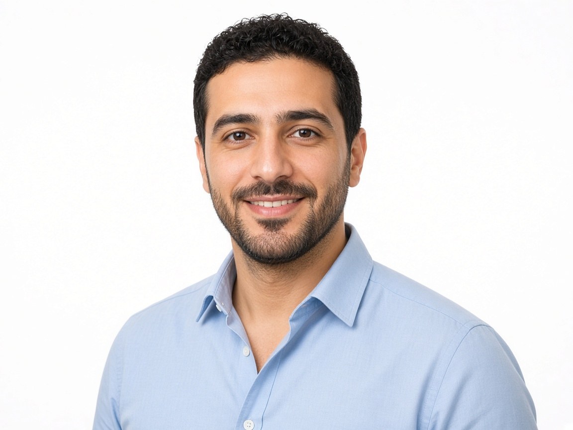 A professional headshot of a man in a light blue shirt on a white studio background